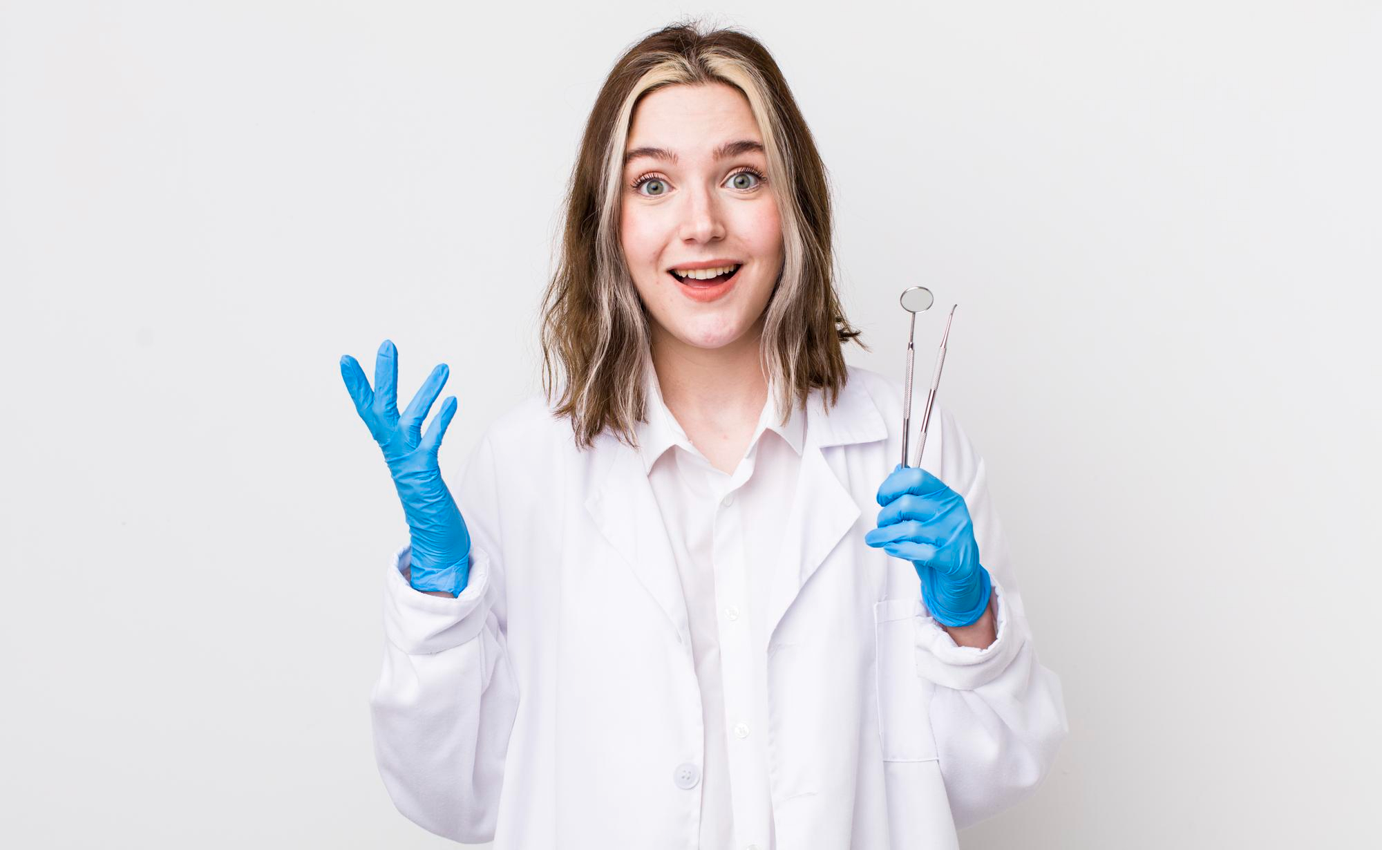 A dentist holding a couple of dental instruments with a surprised as well as inviting expression